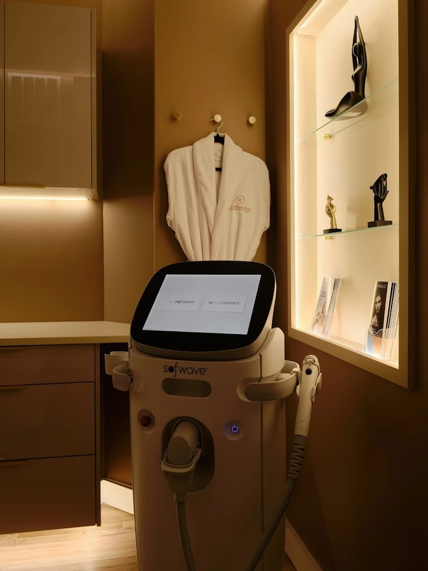 Sofwave body treatment device in a luxury treatment room with illuminated shelving and La Réserve branded robe